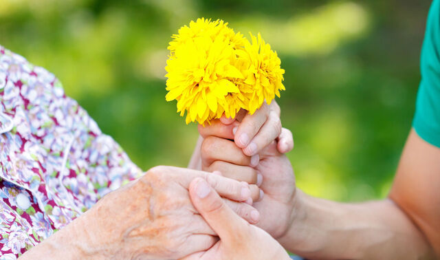 Eine Seniorin kriegt von einer anderen Person einige Blumen in die Hand gedrückt. 